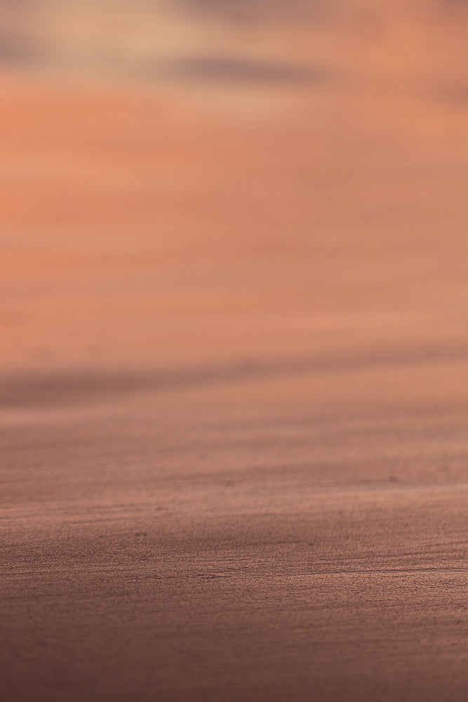 A close-up, abstract shot of a textured surface with horizontal lines. The colors are muted, ranging from a warm, peachy orange in the upper portion to a darker, reddish-brown in the lower portion.
