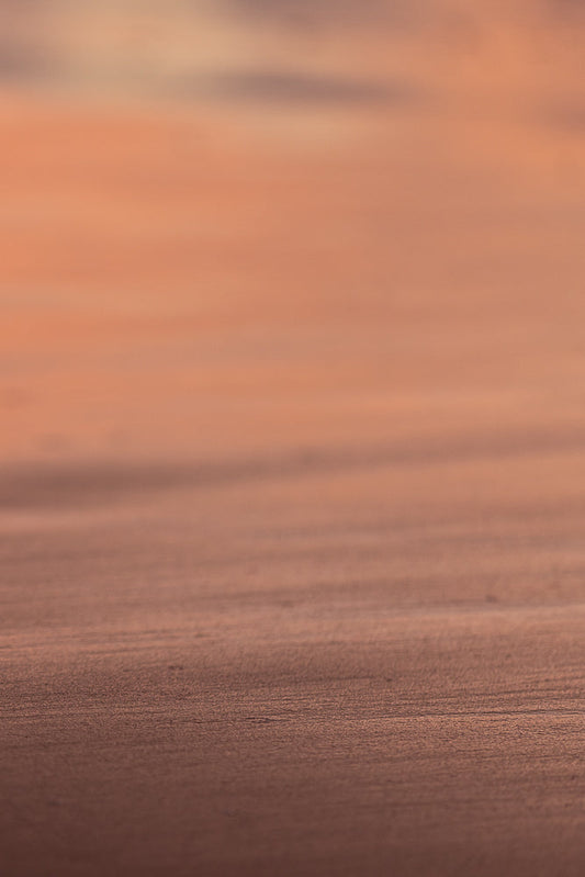 A close-up, abstract shot of a textured surface with horizontal lines. The colors are muted, ranging from a warm, peachy orange in the upper portion to a darker, reddish-brown in the lower portion.