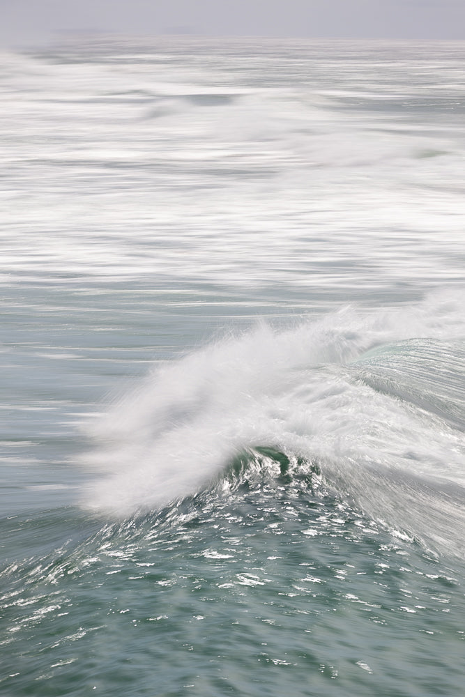 An abstract, impressionistic view of the ocean with a wave breaking in the foreground. The water is rendered in soft, blurred lines of white and green, creating a sense of movement and tranquility.