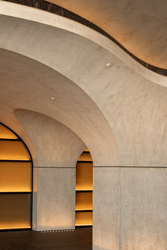 A modern architectural interior with curved concrete arches and warm, amber lighting emanating from recessed alcoves.