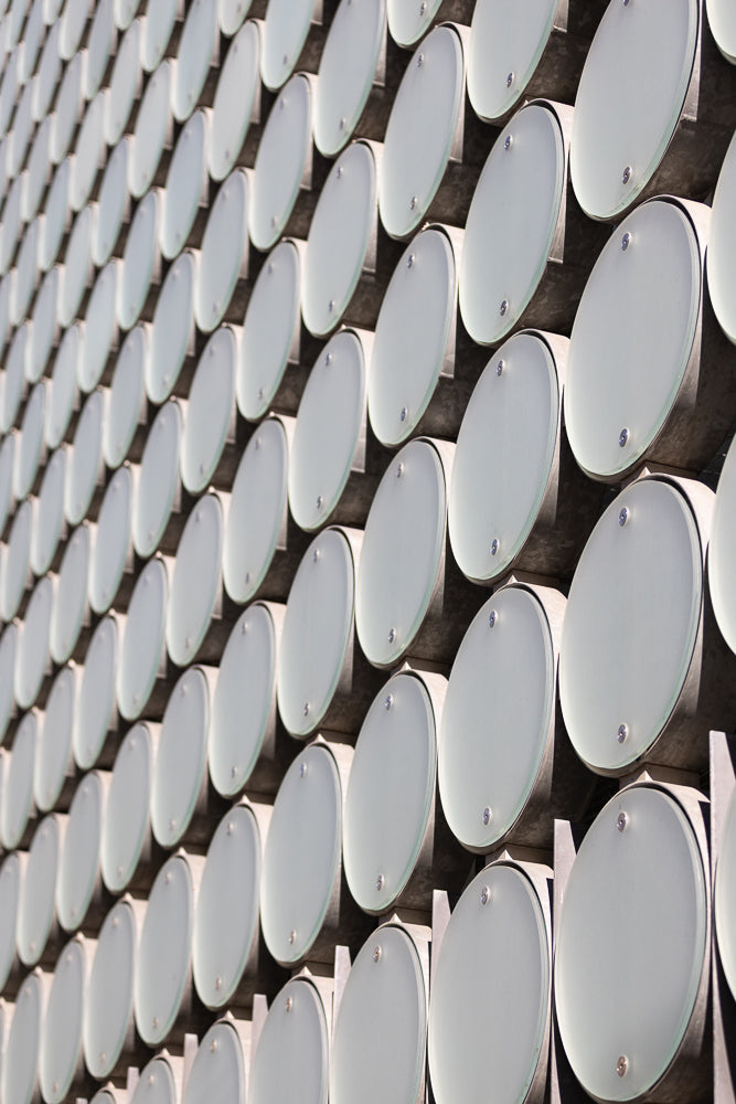 A close-up, angled view of a building facade covered in a repeating pattern of large, oval, frosted glass panels. The panels are attached to a dark, textured background with visible metal fixtures.