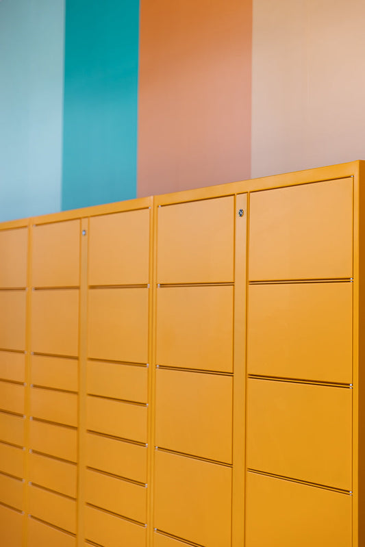 A row of bright orange lockers with silver locks is shown against a wall with vertical stripes of teal, peach, and pale pink.