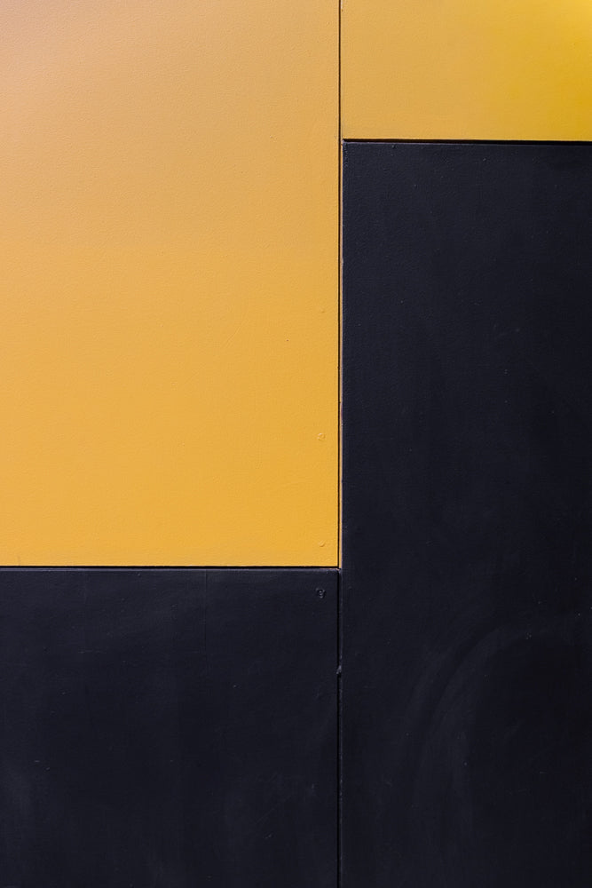 Abstract geometric pattern of a large yellow rectangle on the left, meeting a dark blue rectangle on the right. The two colors meet at a vertical line, with the yellow rectangle also meeting a dark blue rectangle horizontally below it.