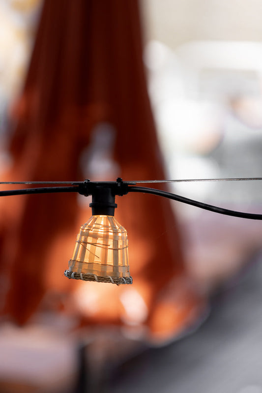 A single Edison-style bulb hangs from a wire, encased in a woven bamboo shade. The warm light illuminates the intricate weave of the shade, creating a cozy atmosphere.