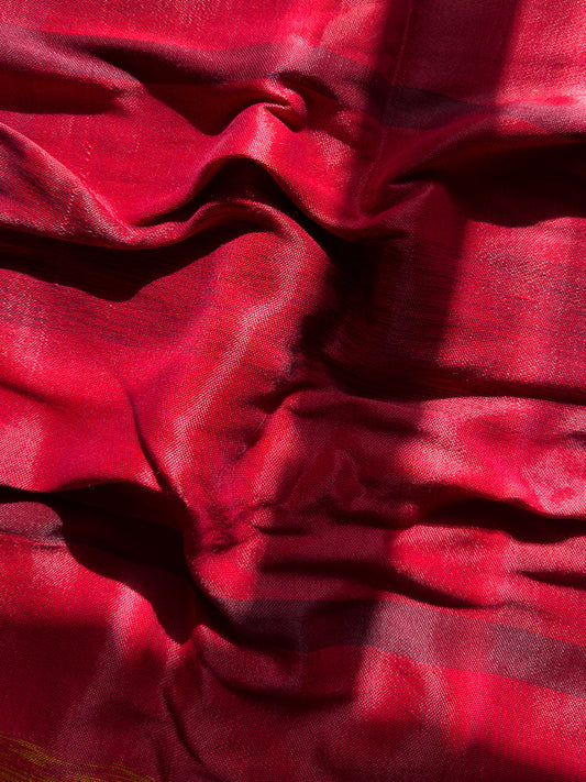 A close-up shot of a red fabric with a textured weave. The fabric is draped and folded, creating shadows and highlights that emphasize its texture and sheen. The lighting suggests it is outdoors or near a window.