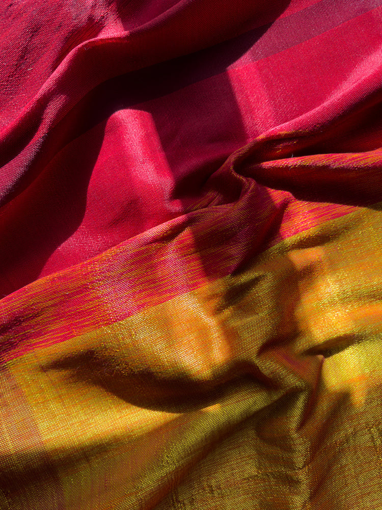 A close-up shot of a richly textured fabric with a gradient of colors from deep red to vibrant yellow and orange. The fabric is draped and folded, creating shadows and highlights that emphasize its weave and sheen.