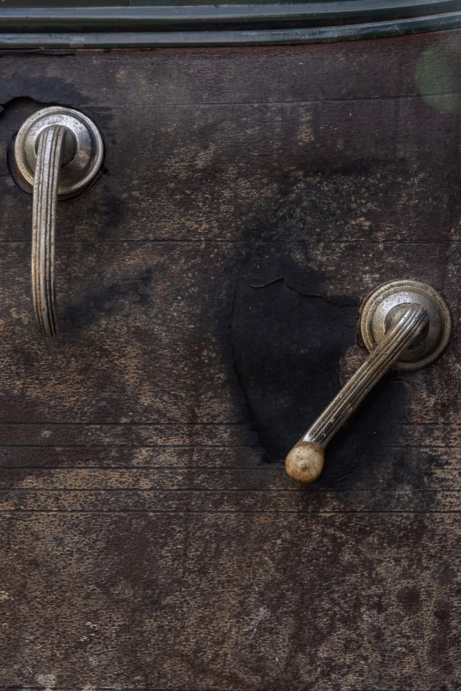 Two vintage metal door handles on a dark, textured surface. The handle on the left is upright, while the one on the right is angled downwards.
