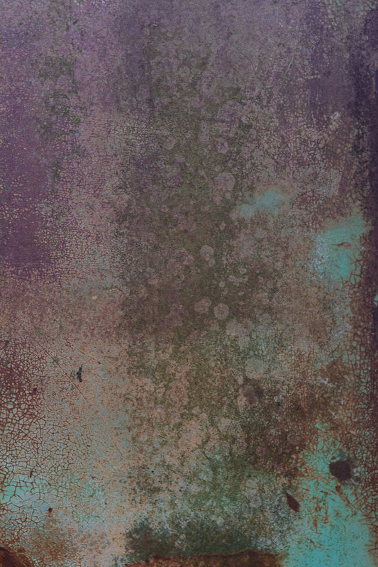 A close-up, abstract view of a weathered surface with peeling paint in shades of purple, green, and brown. The texture is characterized by fine cracks and irregular patches, suggesting age and decay.