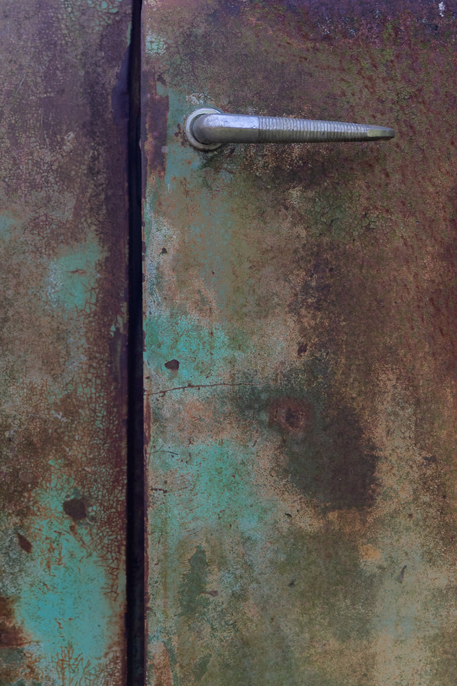 A weathered car door with green and brown rusty texture and old handle