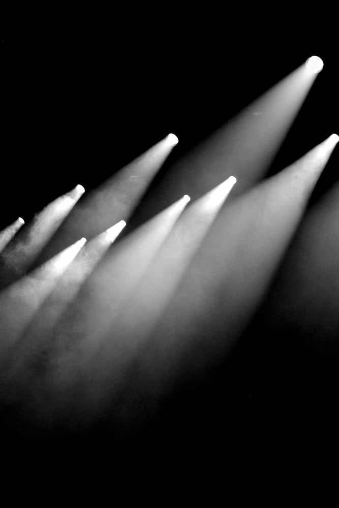 Several bright white spotlights cut through a dark, smoky atmosphere, creating visible beams of light that fan out across the frame.