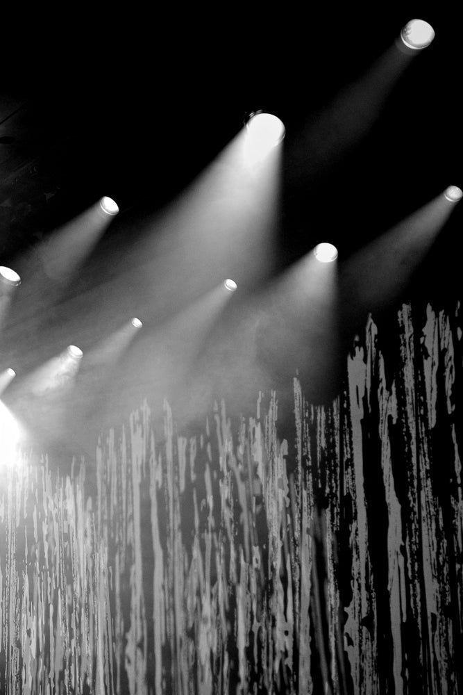 Several spotlights shine down through a smoky atmosphere onto a textured stage curtain.