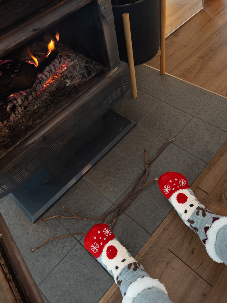 A person's feet wearing festive, fuzzy socks with a polar bear design are resting near a fireplace with a warm fire burning.