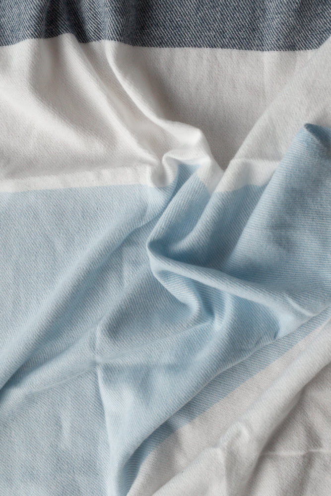 A close-up shot of a soft, wrinkled fabric with horizontal stripes in dark blue, white, and light blue. The texture of the weave is visible, and the fabric is draped in a way that creates shadows and highlights.