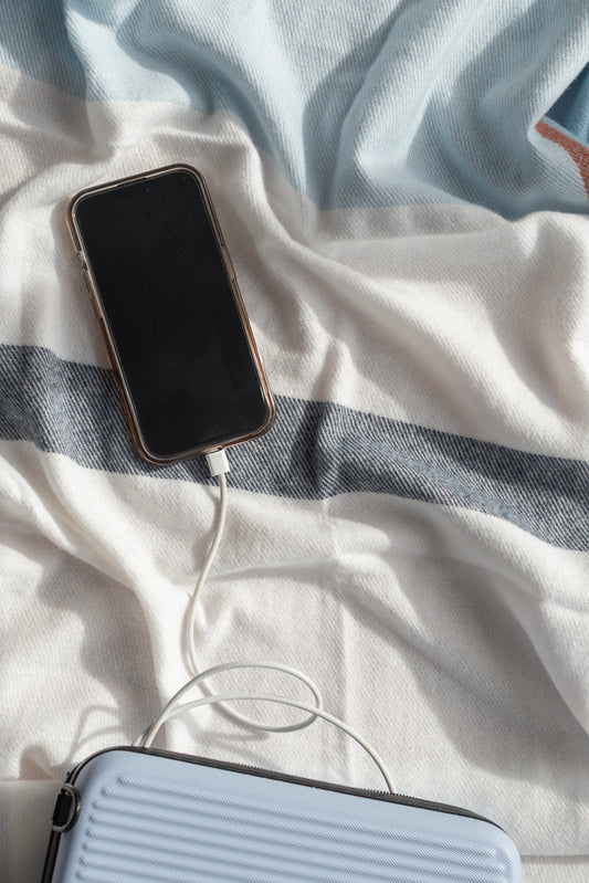A smartphone is charging on a striped blanket. A light blue case is visible at the bottom of the frame.