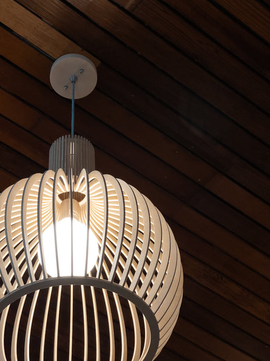 A modern, spherical pendant light fixture made of light-colored wood slats hangs from a white ceiling mount against a dark wood paneled ceiling.