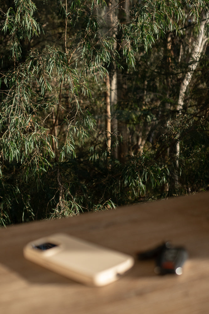 A smartphone and car keys rest on a wooden surface, with a blurred background of eucalyptus trees and foliage.