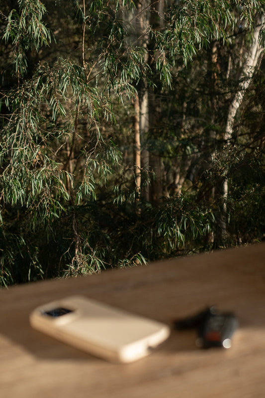 A smartphone and car keys rest on a wooden surface, with a blurred background of eucalyptus trees and foliage.