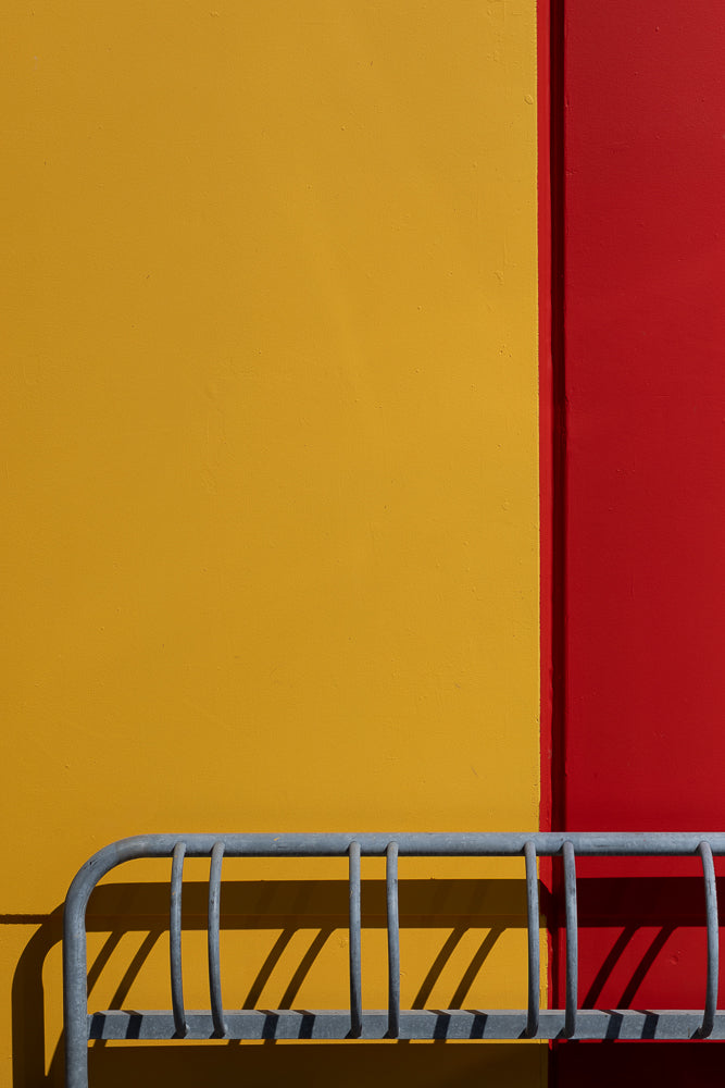 Metal railing casting shadows on vibrant yellow and red wall