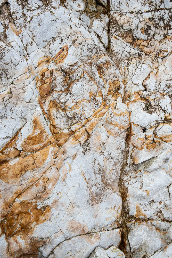 Close-up of a textured rock face with intricate cracks and veins of orange and brown minerals running through the predominantly white and grey stone.