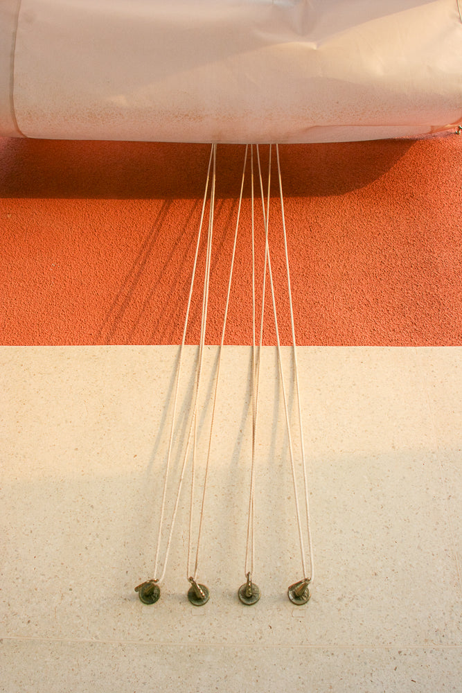 A close-up shot shows four white cords hanging vertically against a textured orange and cream wall. Each cord has a small, round, metallic weight attached to its end.