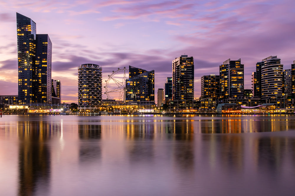 Magical purple sunset over calm, smooth water with buildings and lights reflecting at Dockalnds in Melbourne