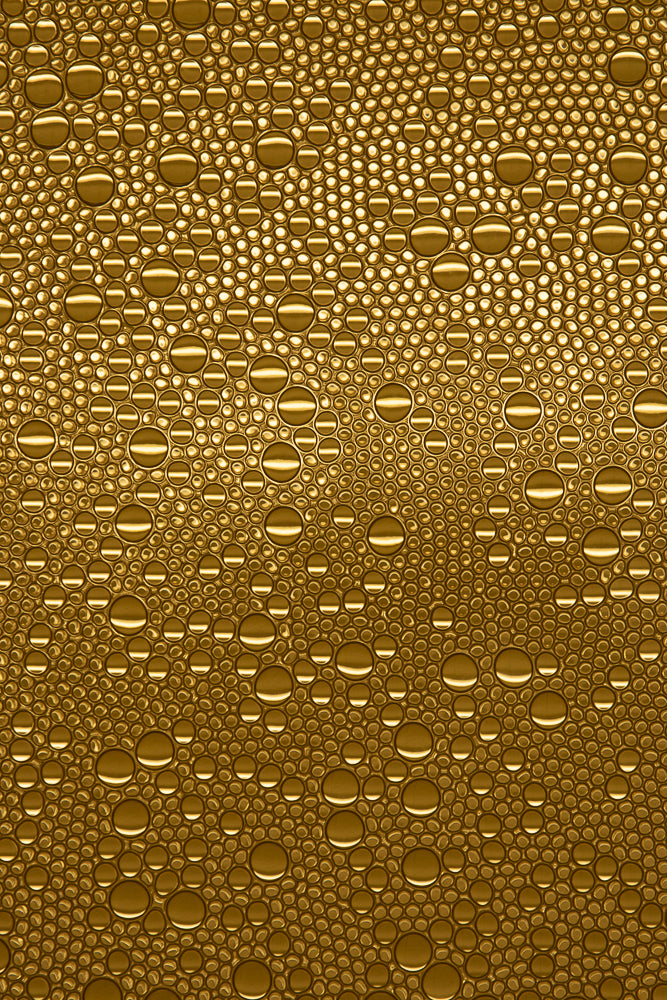 A close-up, abstract view of many golden bubbles of varying sizes, tightly packed together. The bubbles have a glossy, reflective surface with bright highlights.