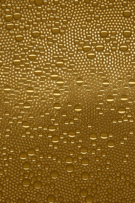 A close-up, abstract view of many golden bubbles of varying sizes, tightly packed together. The bubbles have a glossy, reflective surface with bright highlights.