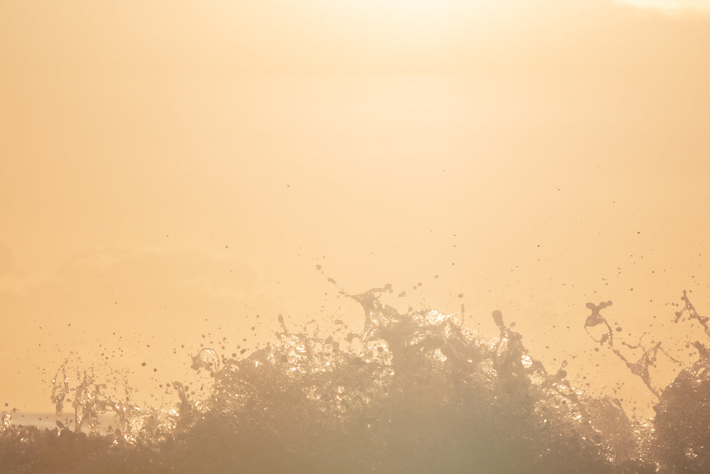 A close-up shot of a water splash against a soft, peachy-orange background. The water is frozen in motion, with droplets and foam catching the light.