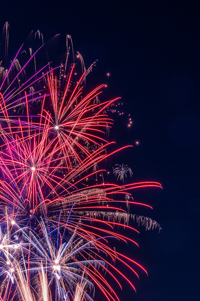 A vibrant display of fireworks illuminates the night sky with streaks of red, pink, and white light against a dark blue background.