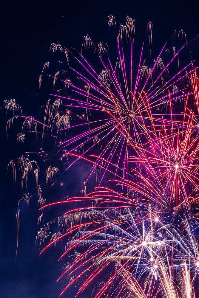 A vibrant display of fireworks illuminates the night sky with streaks of red, pink, and white light against a dark blue background.