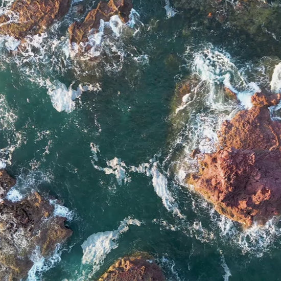 Aerial top-down view of rock formations in green ocean, fly down