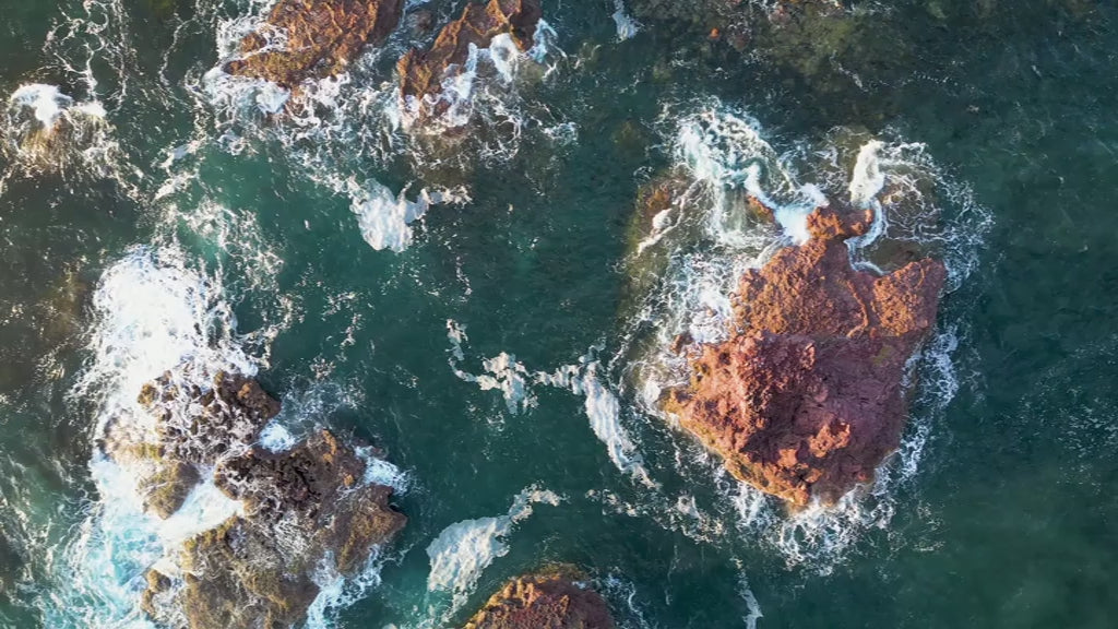 Aerial top-down view of rock formations in green ocean, fly down