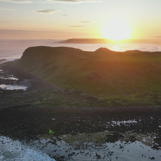 Aerial of a coastline point with sunrise, fly towards the cliff