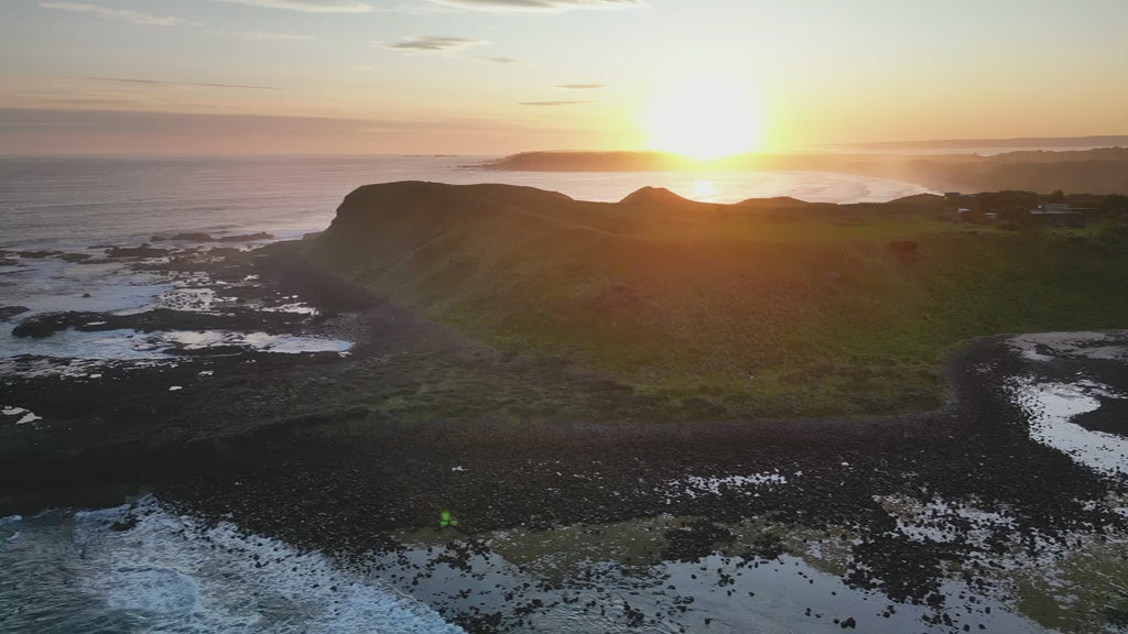 Aerial of a coastline point with sunrise, fly towards the cliff