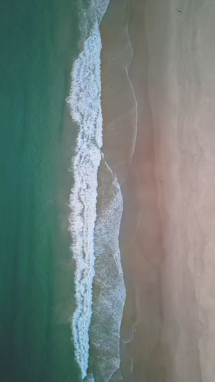 Majestic aerial top down view of turquoise ocean waves gently breaking on a sandy shore. Soothing and beautiful natural scene of the coastline