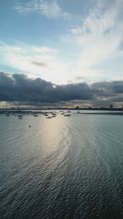 Serene St Kilda marina with sailboats floating peacefully under cloudy sunset sky, capturing tranquil maritime landscape bathed in golden light and Melbourne in background