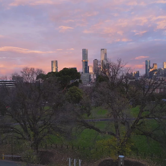 Aerial view of Melbourne skyline at sunrise, flying up from parkland