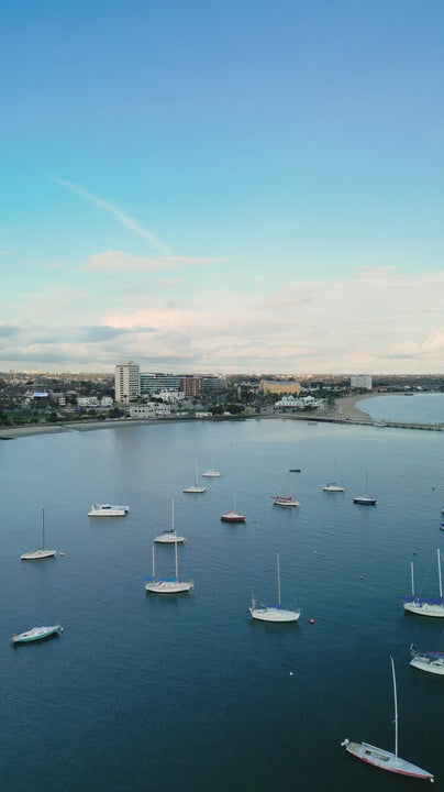 Aerial fly over boats in marina towards St Kilda bayside with blue sky