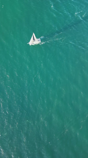 White sailboat gliding smoothly over rippled turquoise ocean waters, capturing nautical freedom and serene maritime adventure from aerial perspective