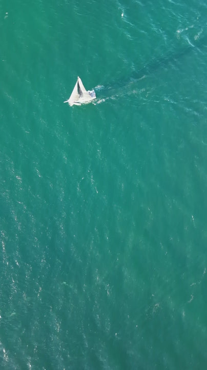 White sailboat gliding smoothly over rippled turquoise ocean waters, capturing nautical freedom and serene maritime adventure from aerial perspective