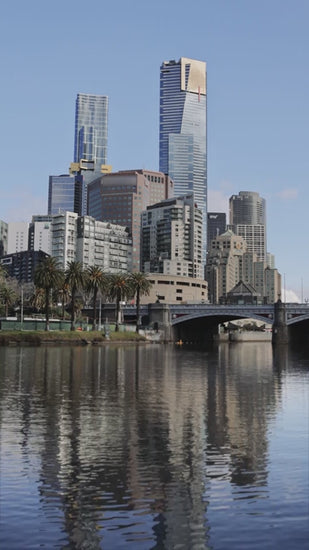 Melbourne city skyline reflecting on Yarra River, with Princes Bridge and modern skyscrapers mirroring in calm water under clear blue sky