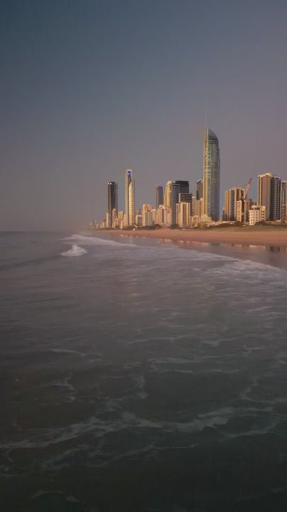 Soft ocean waves rolling towards the gold coast skyline at dawn, creating a peaceful and scenic view