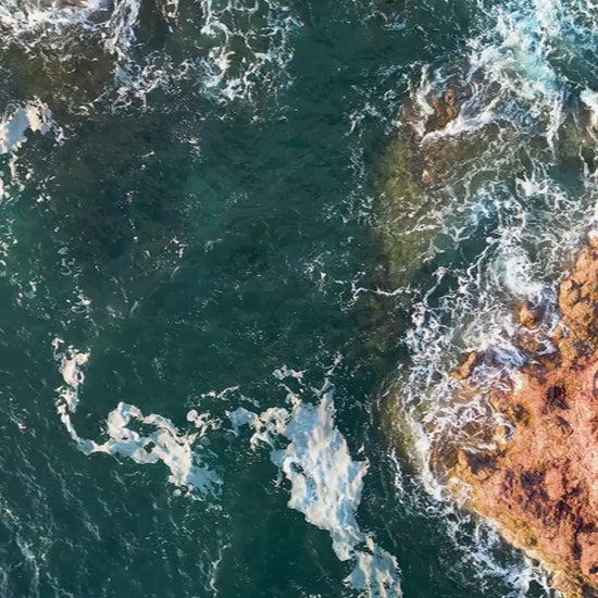 Aerial top-down view of large rock formations in green ocean, fly up