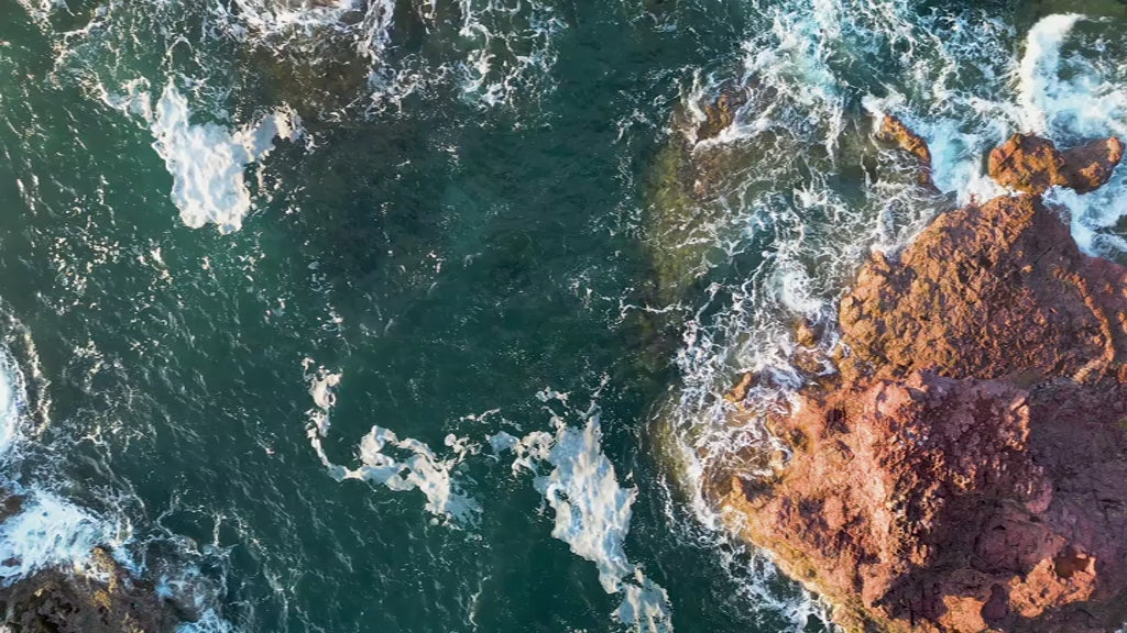 Aerial top-down view of large rock formations in green ocean, fly up