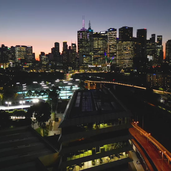 Melbourne skyline over Tennis Centre at sunset, fly up view
