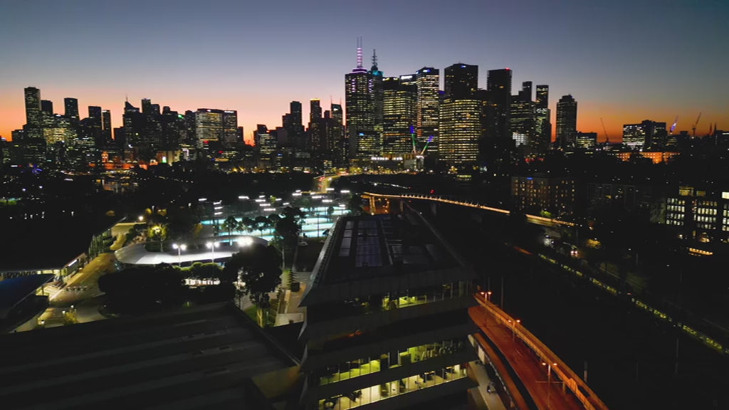 Melbourne skyline over Tennis Centre at sunset, fly up view