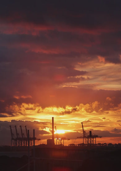 Orange and purple sunset over an industrial port, featuring silhouetted cranes and vibrant sky in Port Melbourne
