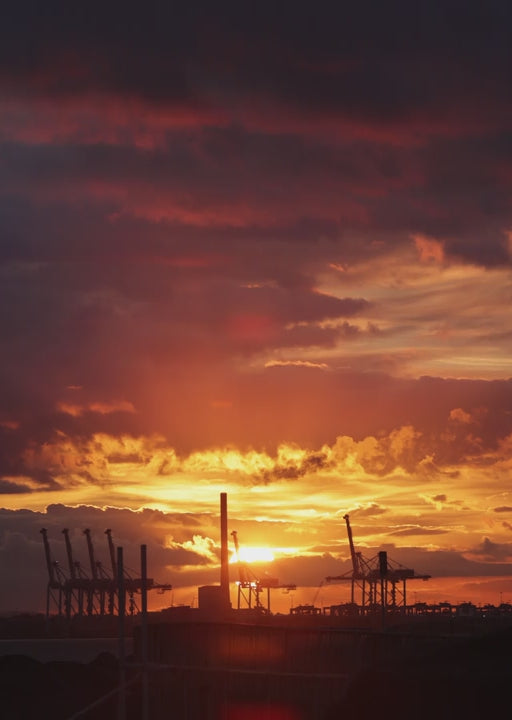 Orange and purple sunset over an industrial port, featuring silhouetted cranes and vibrant sky in Port Melbourne