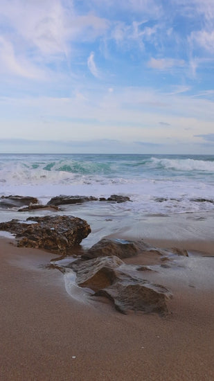 Slow motion of gentle waves rolling on rocky sandy beach under blue sky, creating peaceful seascape