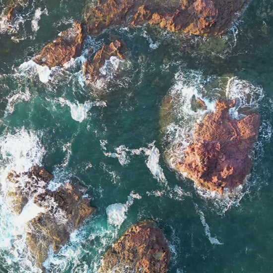Aerial top-down view of large rocks waves crashing in green sea